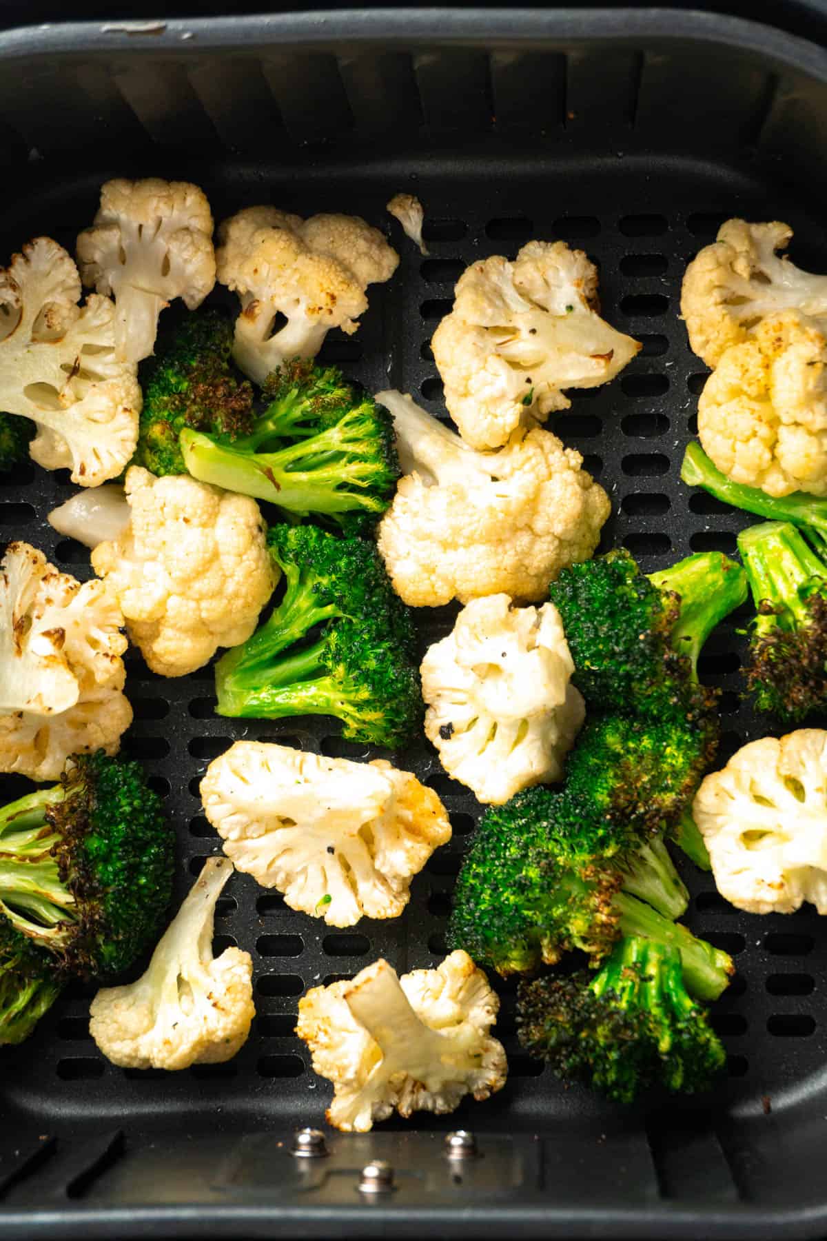 Close up of the broccoli and cauliflower in the air fryer basket after being cooked. 