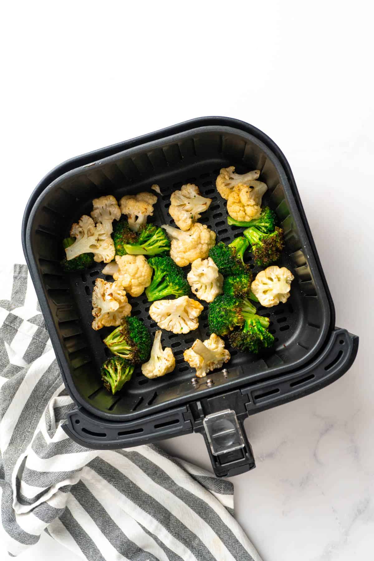 Cooked and crispy broccoli and cauliflower in the air fryer basket. 