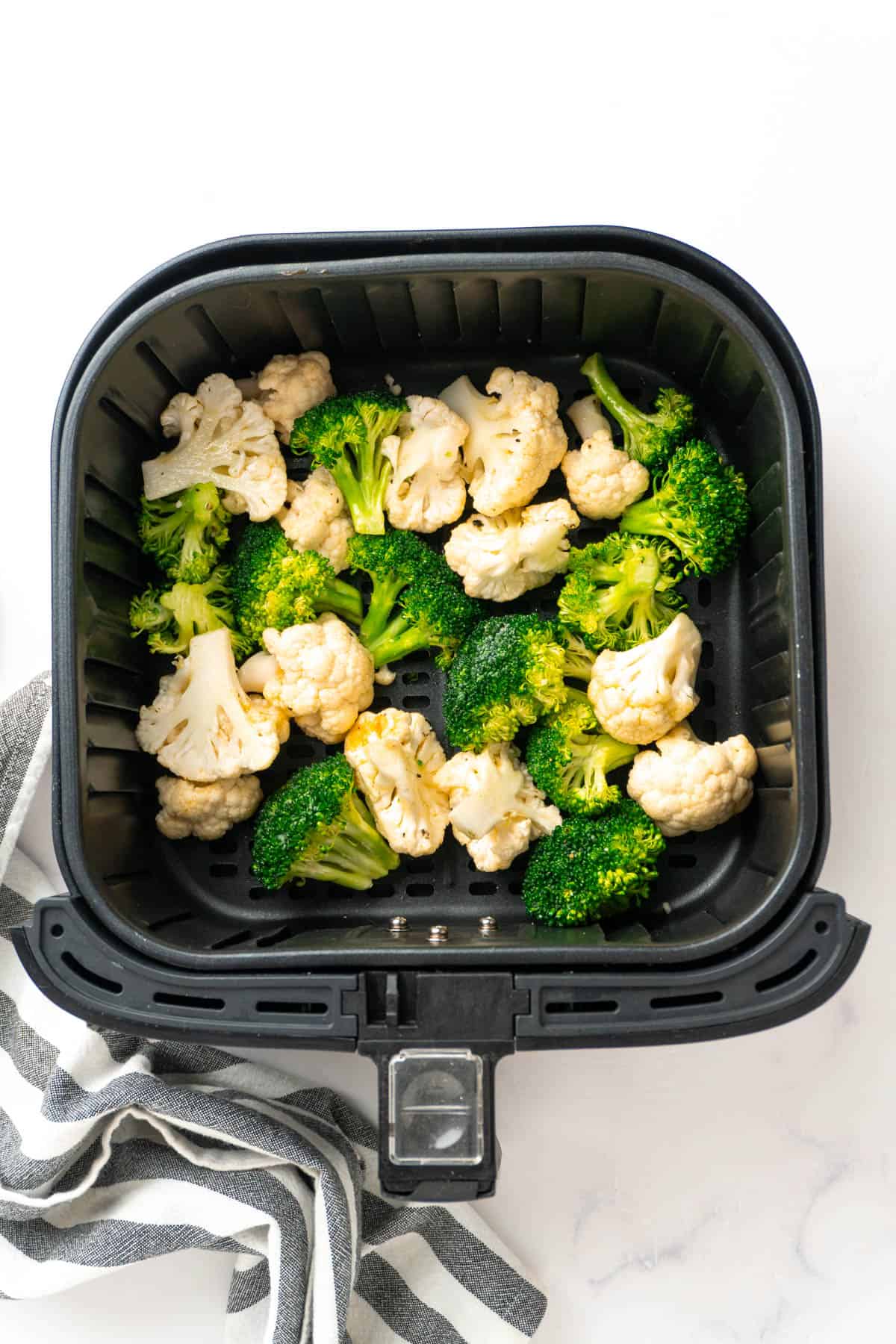 Seasoned broccoli and cauliflower are spread out in a single layer in the air fryer basket. 
