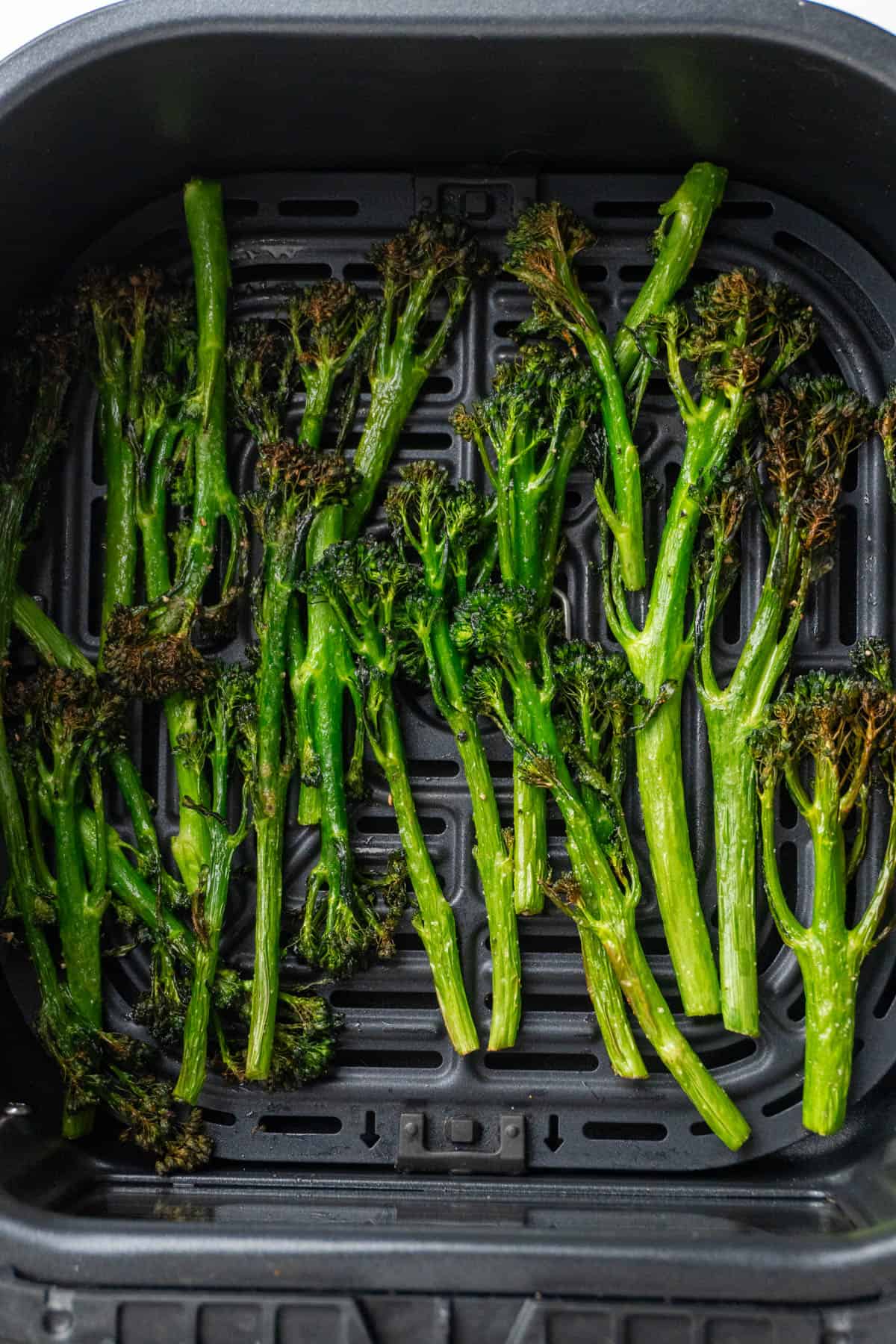 Crispy and slightly browned broccolini in the air fryer basket. 
