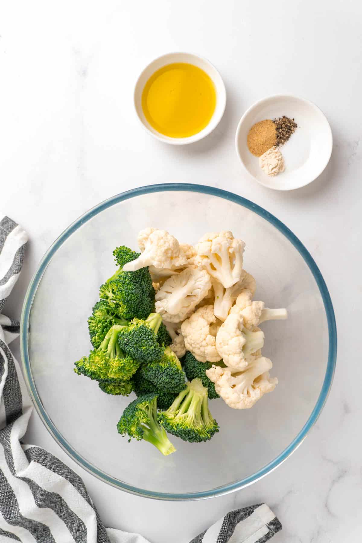Ingredients for the air fryer broccoli and cauliflower laid out on a white background in dishes and bowls. 