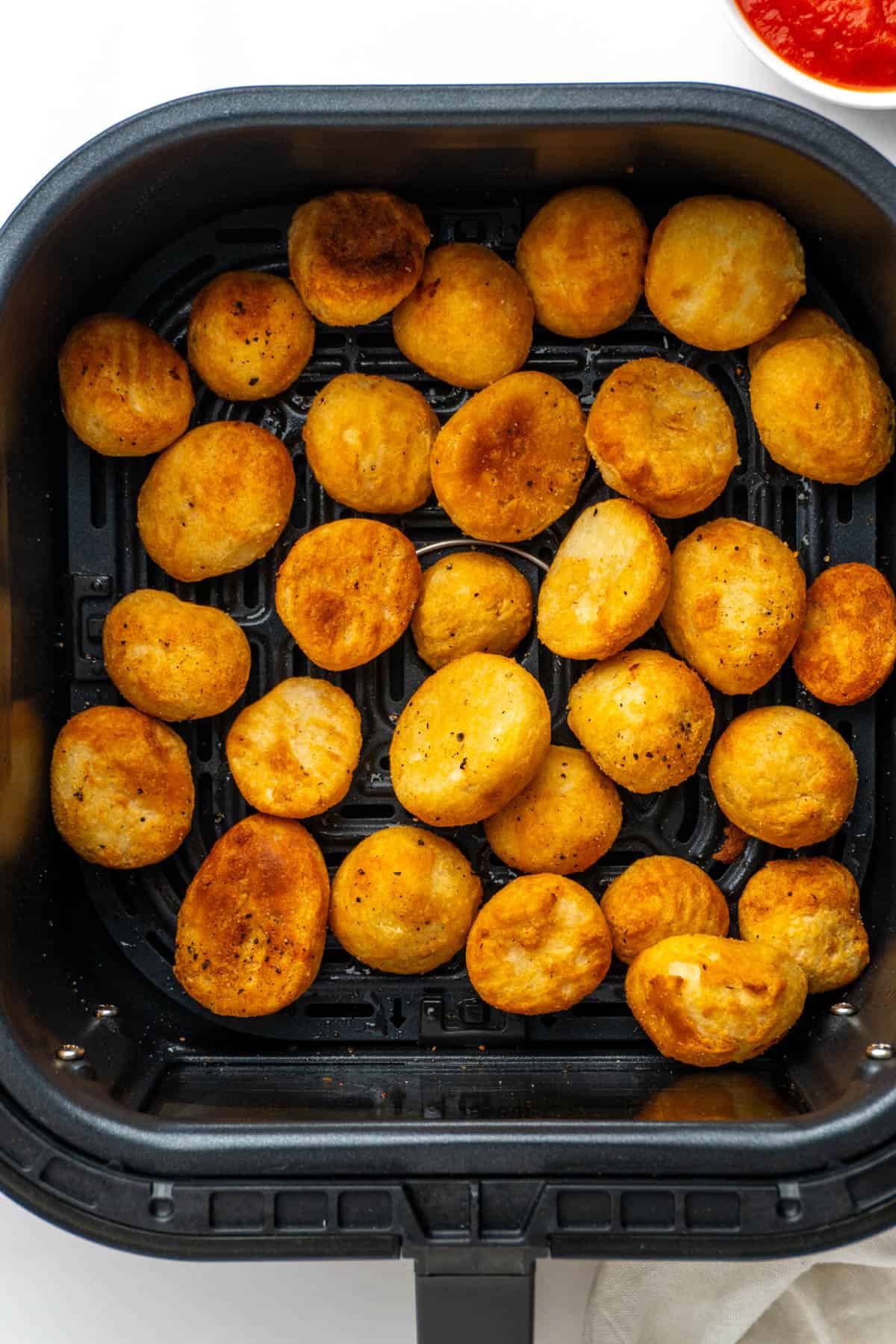 Crispy golden roast potatoes in the air fryer basket after being cooked.