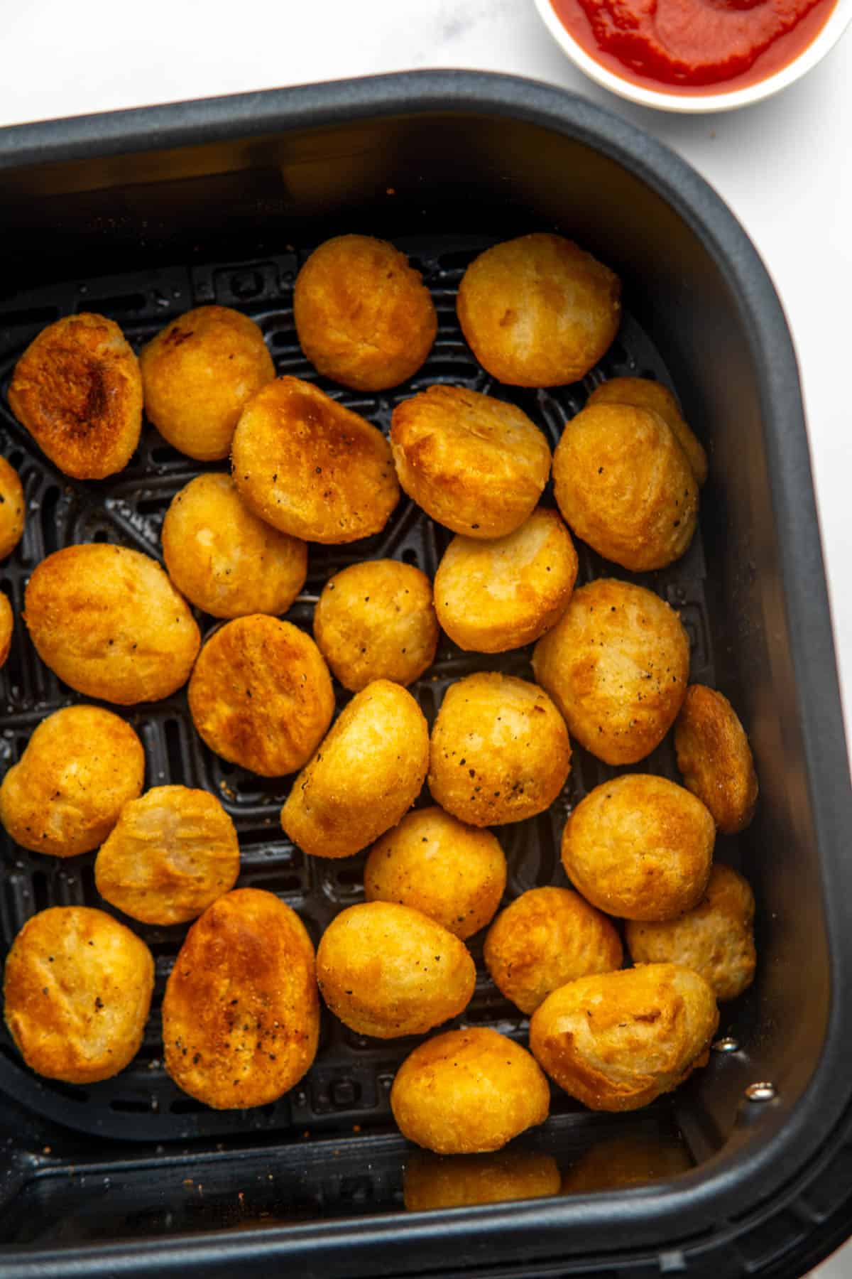 Crispy, golden roast potatoes in the air fryer basket after being cooked.