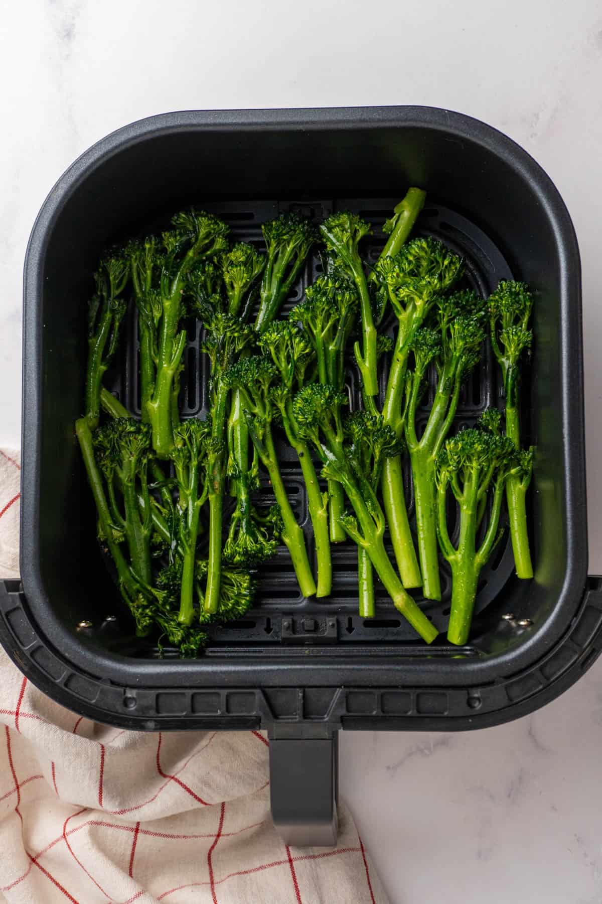 Broccolini arranged in a single layer in the air fryer basket before cooking. 