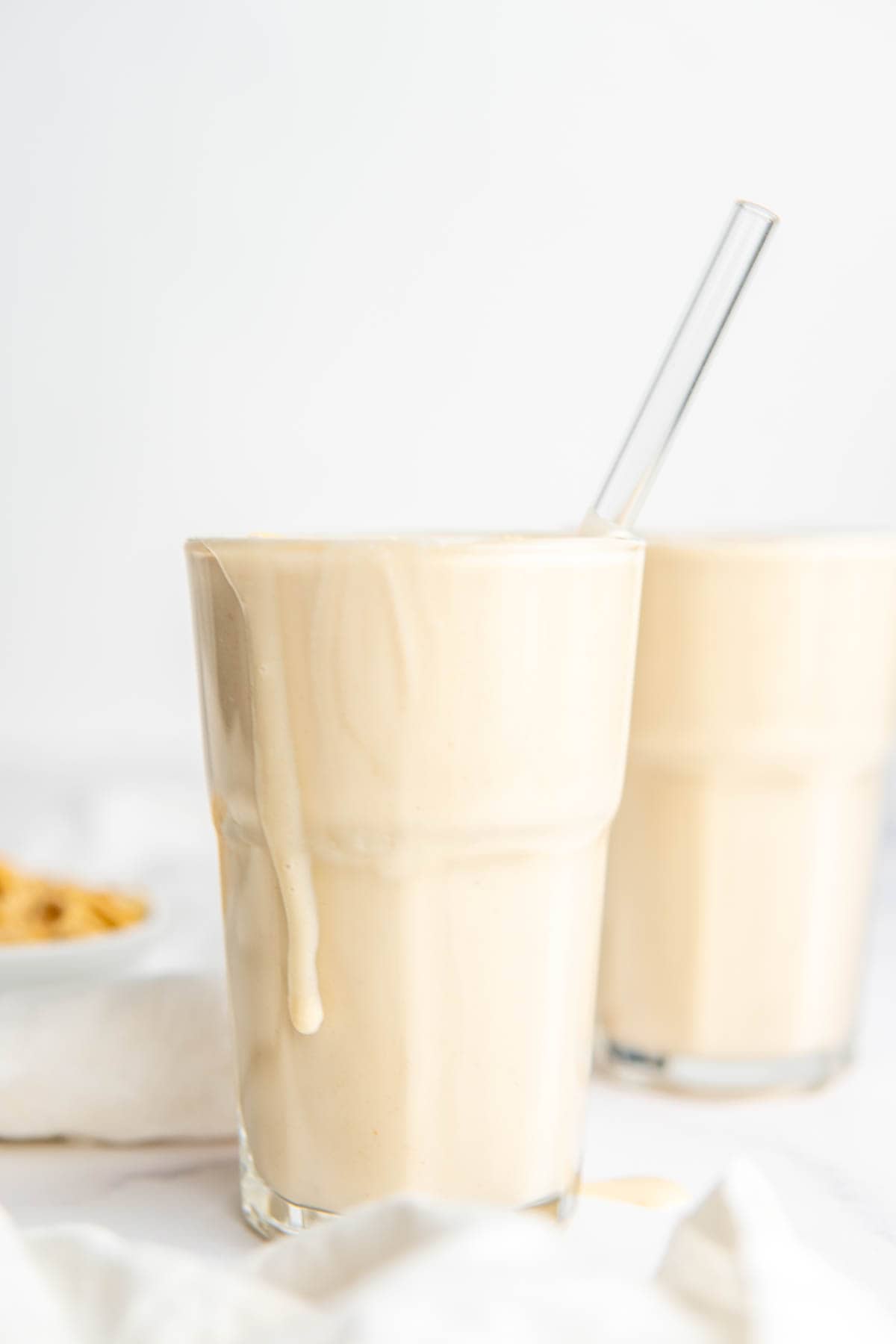A glass full of thick, creamy smoothie with a glass straw sticking out. 